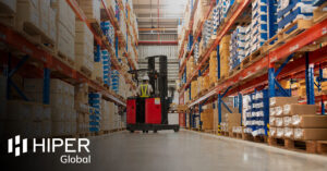 A worker in a forklift loading packed goods in a large distribution warehouse with high shelves - including the HIPER Global logo