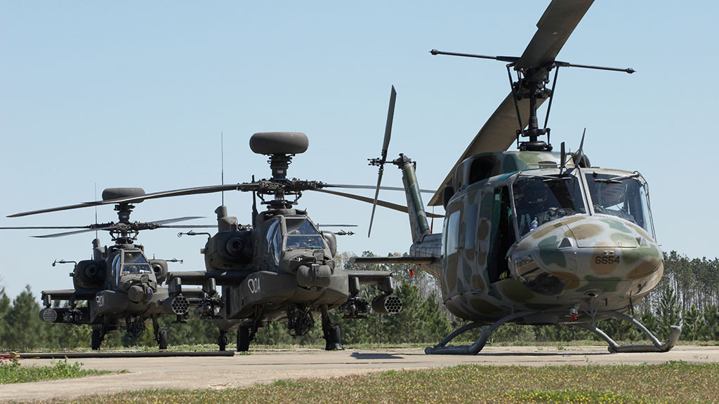 A set of three apache helicopters sit on their helipads, equipped with MIL-STD rugged hardware and CompactPCI technology